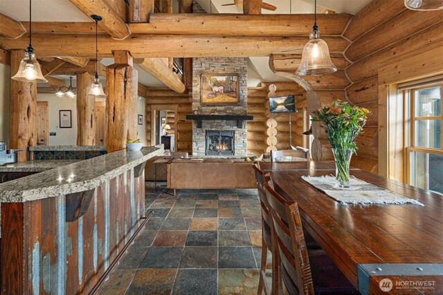 dining space featuring beam ceiling, log walls, a fireplace, and stone tile flooring