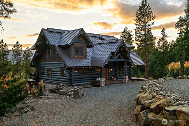 back of property at dusk featuring driveway, a standing seam roof, log siding, and metal roof