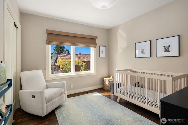 bedroom with baseboards, a crib, and dark wood-type flooring