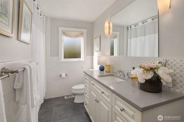 bathroom featuring wainscoting, tile patterned flooring, vanity, toilet, and tile walls