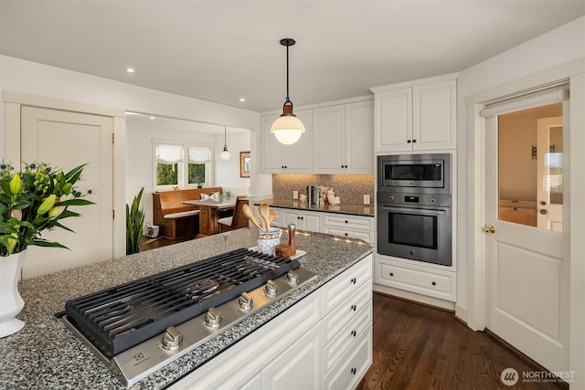 kitchen featuring white cabinets, dark wood-style flooring, dark stone countertops, stainless steel appliances, and decorative backsplash