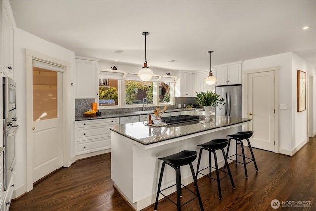 kitchen featuring dark wood-style flooring, white cabinetry, a sink, appliances with stainless steel finishes, and backsplash