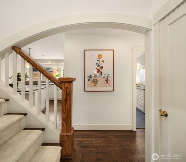 stairs featuring arched walkways, baseboards, and wood finished floors