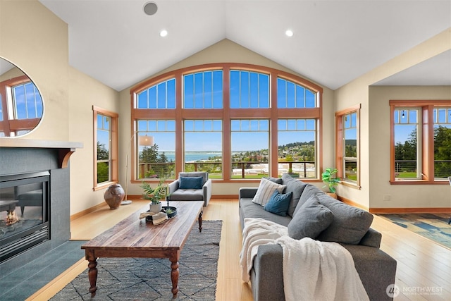 living area featuring wood finished floors, baseboards, a glass covered fireplace, and lofted ceiling