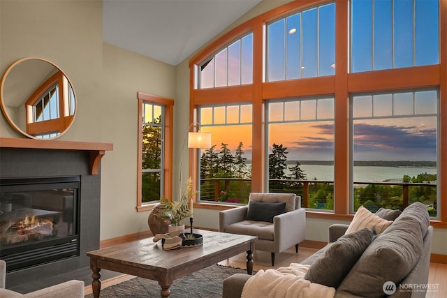 living area with a glass covered fireplace, a water view, vaulted ceiling, and a wealth of natural light