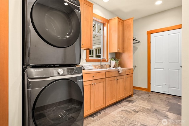 laundry area featuring stacked washer / dryer, cabinet space, a sink, baseboards, and recessed lighting