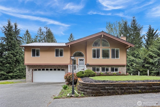 bi-level home with brick siding, a garage, aphalt driveway, and a chimney