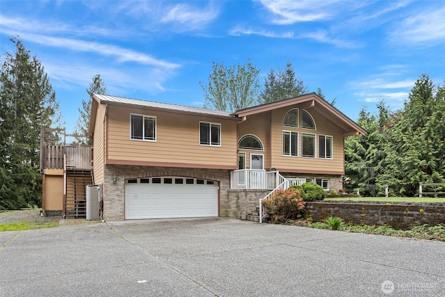 raised ranch featuring a garage, stairs, concrete driveway, and metal roof