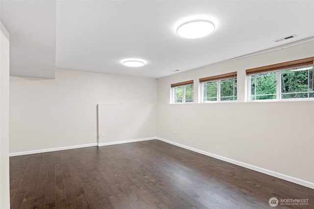 unfurnished room featuring baseboards, dark wood finished floors, and visible vents