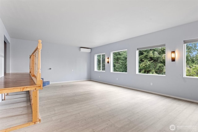 unfurnished living room featuring wood finished floors, a wall mounted AC, a healthy amount of sunlight, and stairway