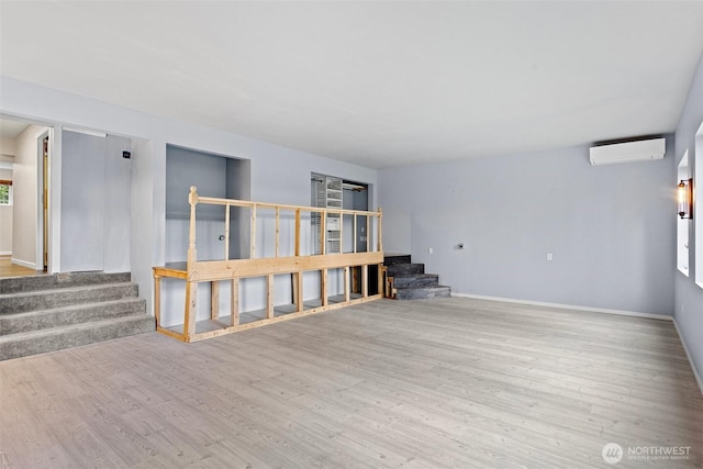 interior space featuring wood finished floors, baseboards, a wall mounted AC, and stairway