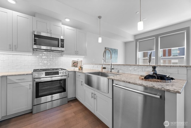 4961 Main St Unit 612, Tacoma, WA 98407 - kitchen with stainless steel appliances, a sink, wood finished floors, decorative backsplash, and light stone counters