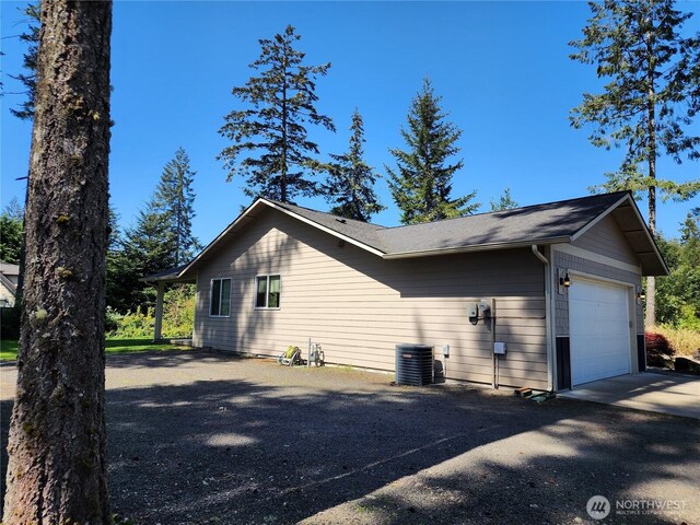 view of side of home with an attached garage, aphalt driveway, and cooling unit