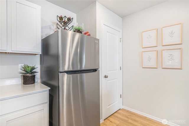 kitchen featuring freestanding refrigerator, baseboards, light countertops, white cabinets, and light wood finished floors