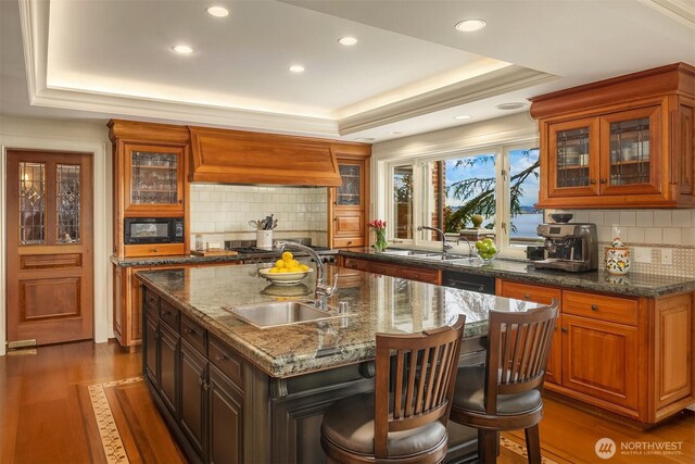 kitchen with a raised ceiling, a sink, black appliances, and custom range hood
