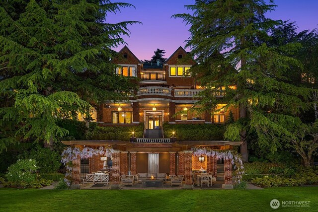 rear view of house with a balcony, brick siding, a patio area, a lawn, and an outdoor fire pit