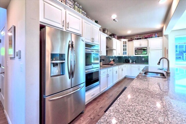 kitchen featuring light stone countertops, appliances with stainless steel finishes, a sink, white cabinetry, and decorative backsplash