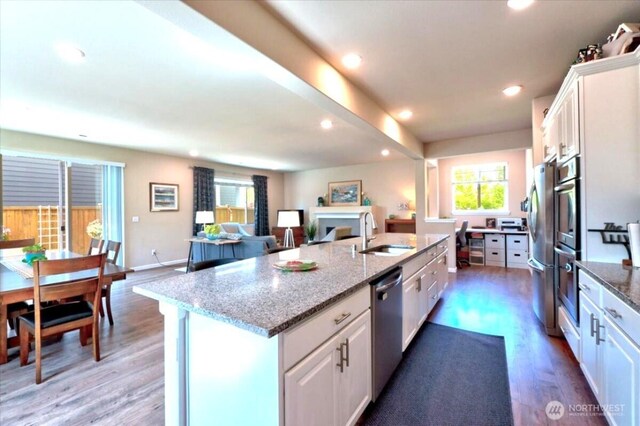 kitchen with appliances with stainless steel finishes, wood finished floors, a sink, white cabinets, and an island with sink