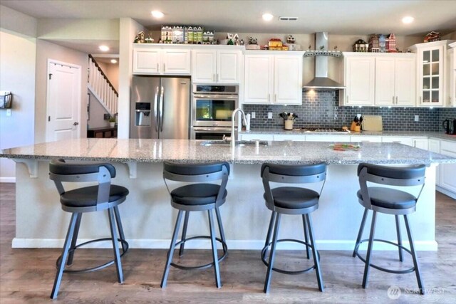 kitchen with baseboards, white cabinets, wall chimney range hood, and stainless steel appliances