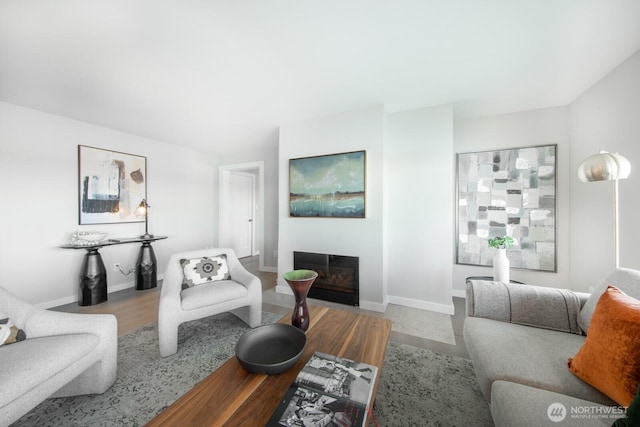 living area with a glass covered fireplace, baseboards, and wood finished floors