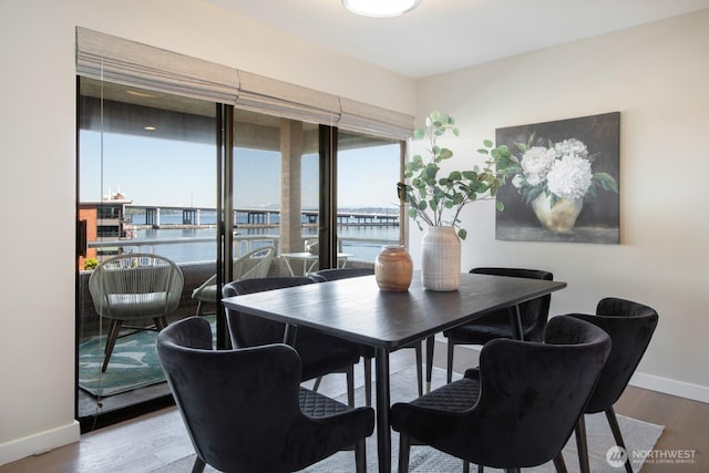 dining area featuring baseboards, a water view, and wood finished floors