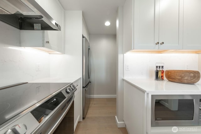 kitchen with appliances with stainless steel finishes, light wood-style floors, light countertops, baseboards, and range hood