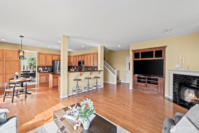 living room featuring a high end fireplace, light wood-style flooring, stairs, and recessed lighting