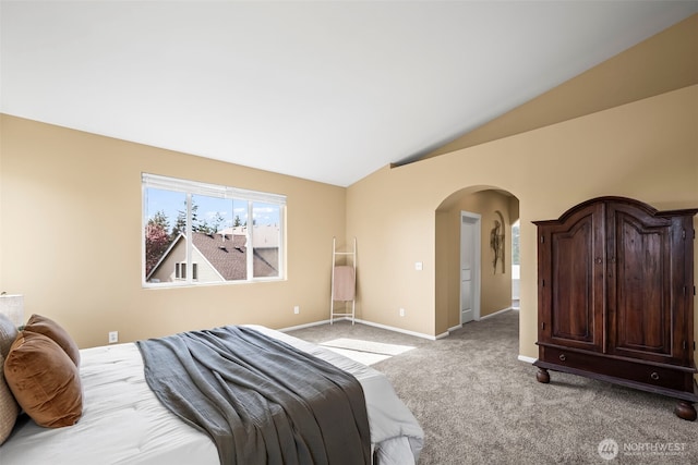 bedroom with light colored carpet, arched walkways, baseboards, and vaulted ceiling