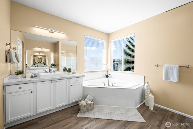 full bathroom with a garden tub, walk in shower, wood finished floors, baseboards, and vanity