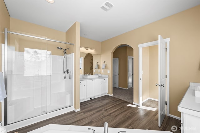 full bath with vanity, baseboards, wood finished floors, visible vents, and a stall shower