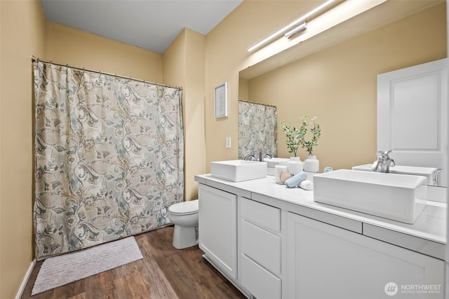 bathroom featuring double vanity, toilet, a sink, and wood finished floors