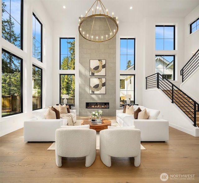 living area featuring a notable chandelier, a fireplace, wood finished floors, a towering ceiling, and stairway