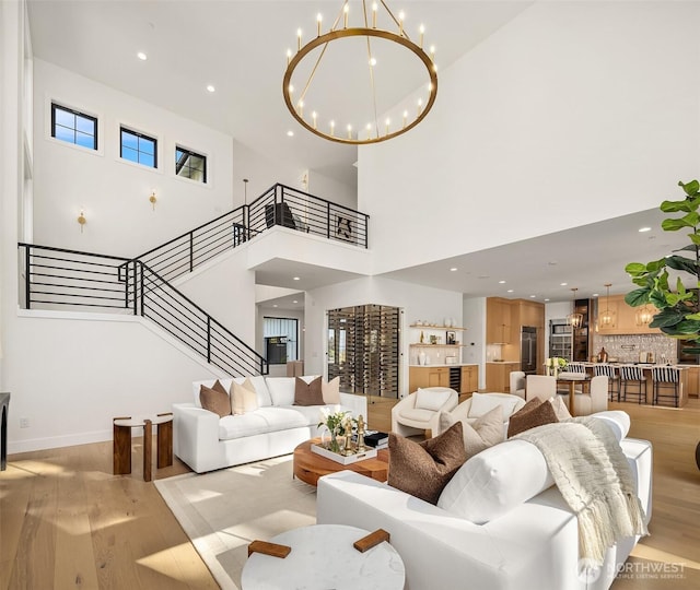 living area featuring a towering ceiling, stairway, light wood finished floors, an inviting chandelier, and recessed lighting