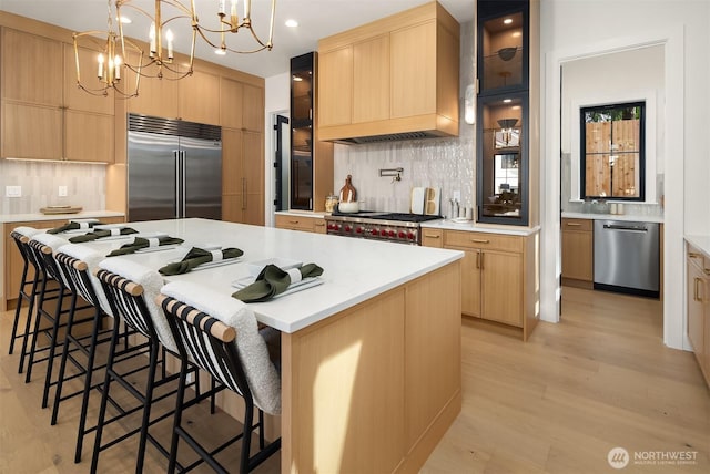 kitchen with light wood-style floors, light countertops, light brown cabinets, decorative backsplash, and premium appliances