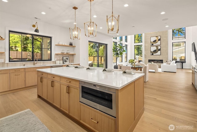 kitchen featuring open shelves, a kitchen island, a fireplace, light wood-style floors, and a sink