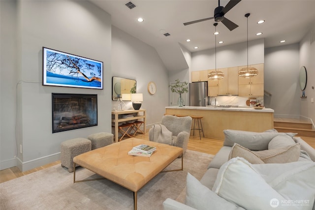 living room with visible vents, a ceiling fan, light wood-style floors, and a glass covered fireplace