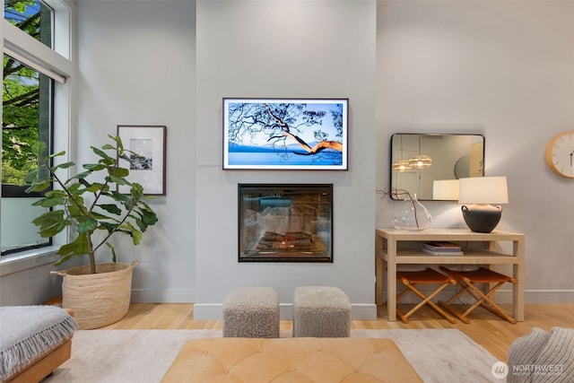 living area featuring a glass covered fireplace, baseboards, wood finished floors, and a towering ceiling