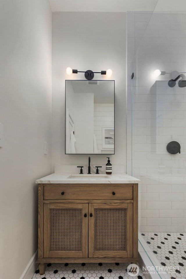 full bath with baseboards, tiled shower, and vanity