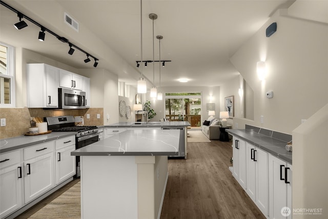 kitchen featuring visible vents, a peninsula, open floor plan, rail lighting, and appliances with stainless steel finishes