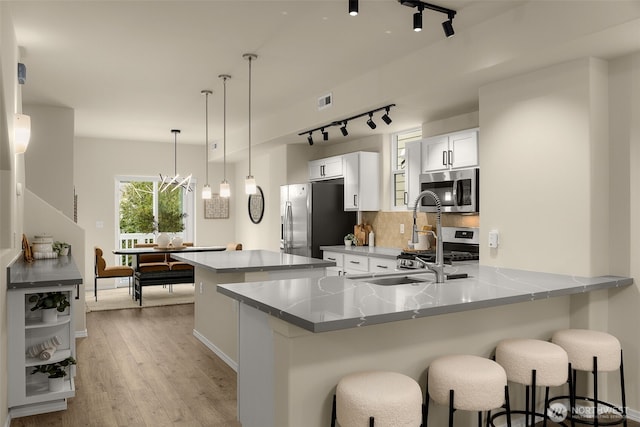 kitchen featuring appliances with stainless steel finishes, rail lighting, light wood-type flooring, a kitchen bar, and backsplash