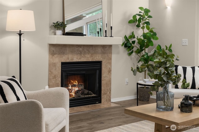 living area with baseboards, a lit fireplace, and wood finished floors