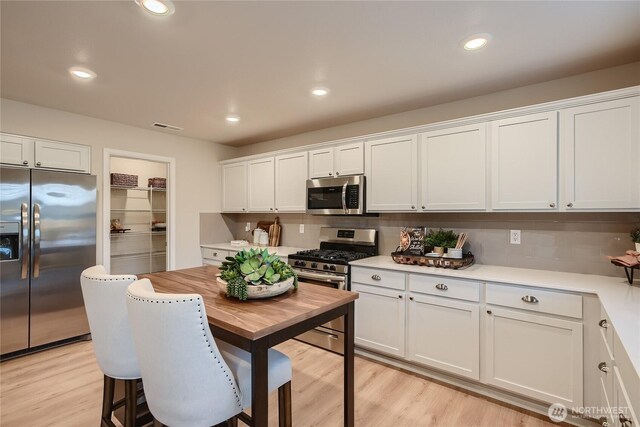kitchen with decorative backsplash, light countertops, white cabinets, light wood finished floors, and stainless steel appliances