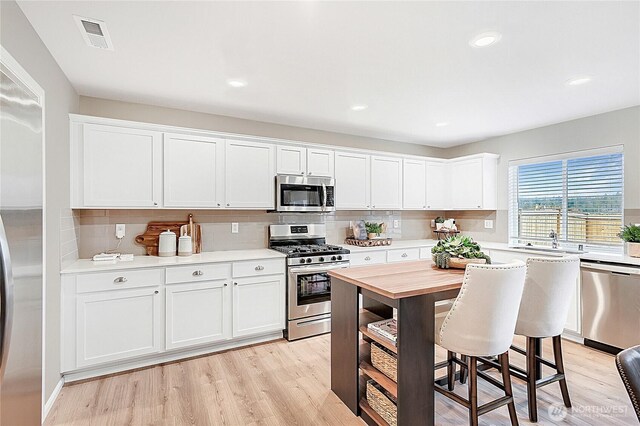 kitchen featuring backsplash, visible vents, a sink, white cabinets, and stainless steel appliances