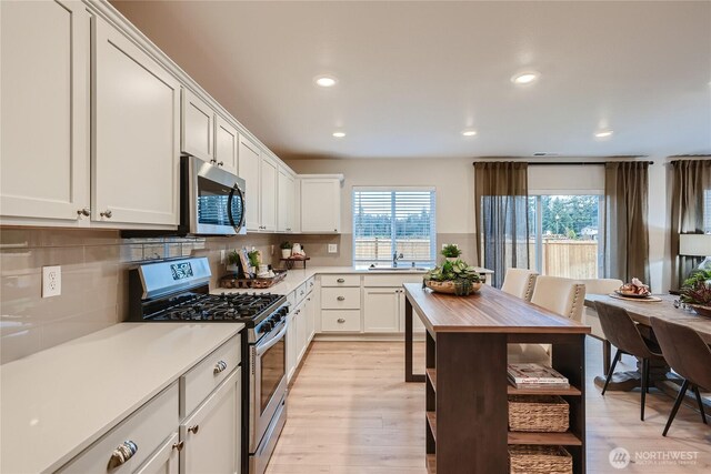 kitchen with light countertops, backsplash, stainless steel appliances, and a wealth of natural light
