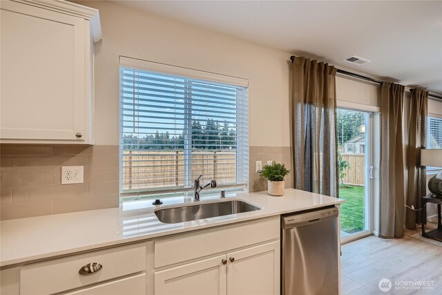 kitchen with a sink, dishwasher, light countertops, decorative backsplash, and visible vents
