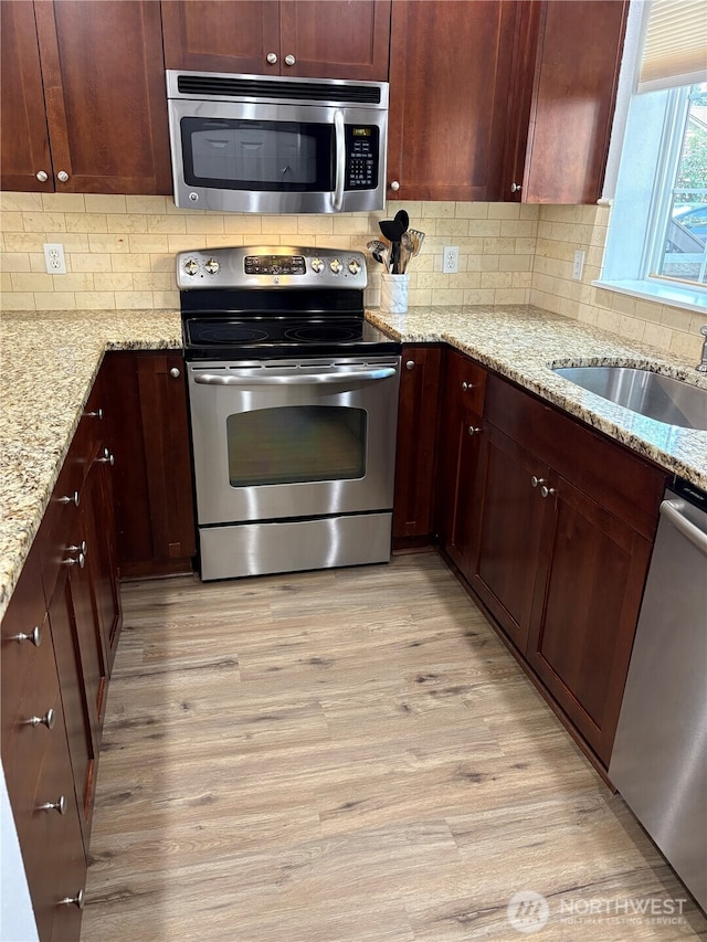 25025 SE Klahanie Blvd Unit L104, Sammamish, WA 98029 - kitchen with light wood-type flooring, light stone counters, a sink, appliances with stainless steel finishes, and backsplash