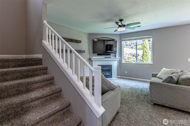 carpeted living area with ceiling fan, a fireplace, stairs, baseboards, and visible vents