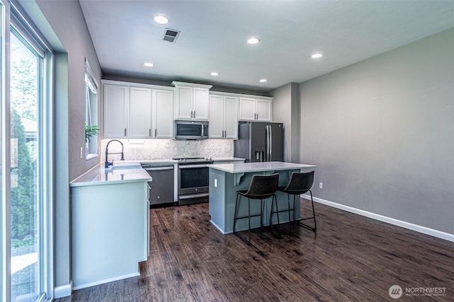 kitchen with a center island, stainless steel appliances, white cabinetry, tasteful backsplash, and visible vents