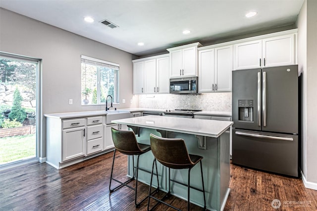 kitchen featuring a breakfast bar, light countertops, stainless steel appliances, backsplash, and visible vents