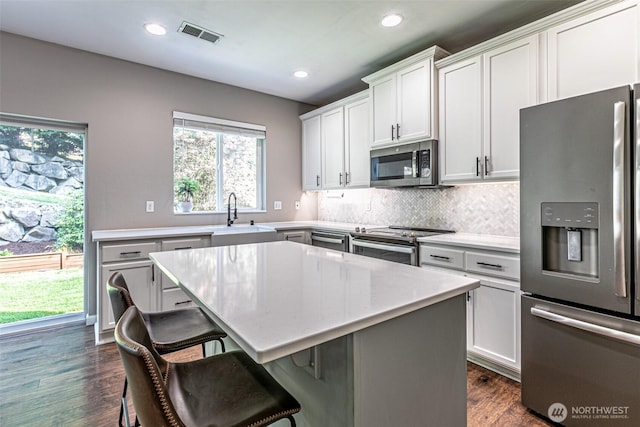 kitchen featuring a sink, a breakfast bar area, stainless steel appliances, decorative backsplash, and visible vents